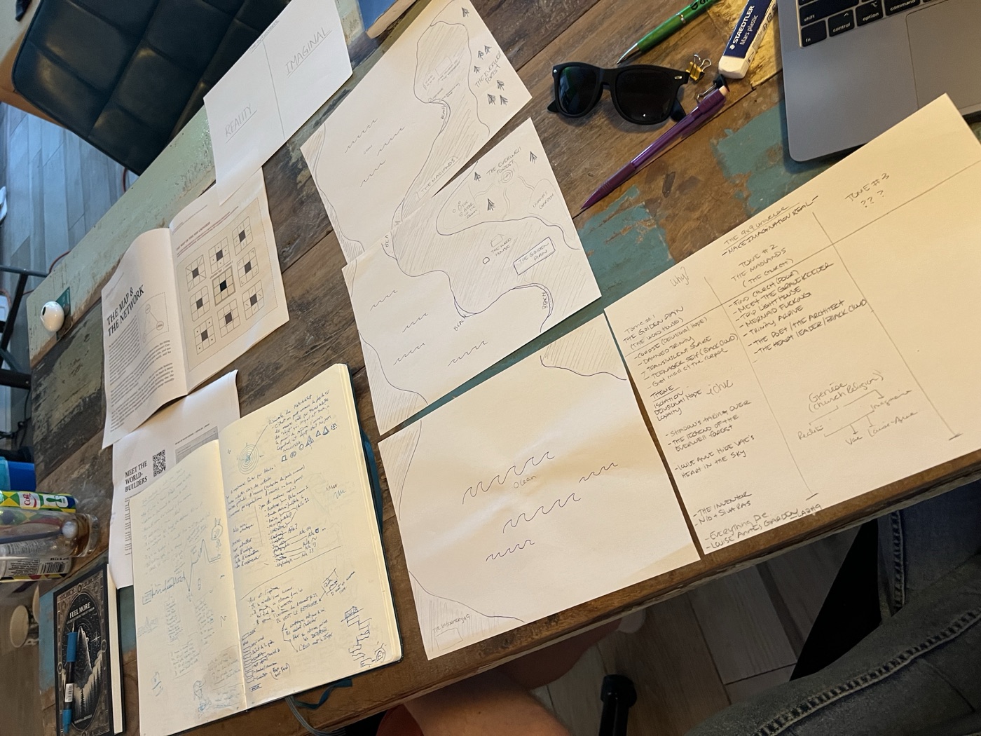 Sketchbooks, maps, and blueprint drafts spread across a worktable.