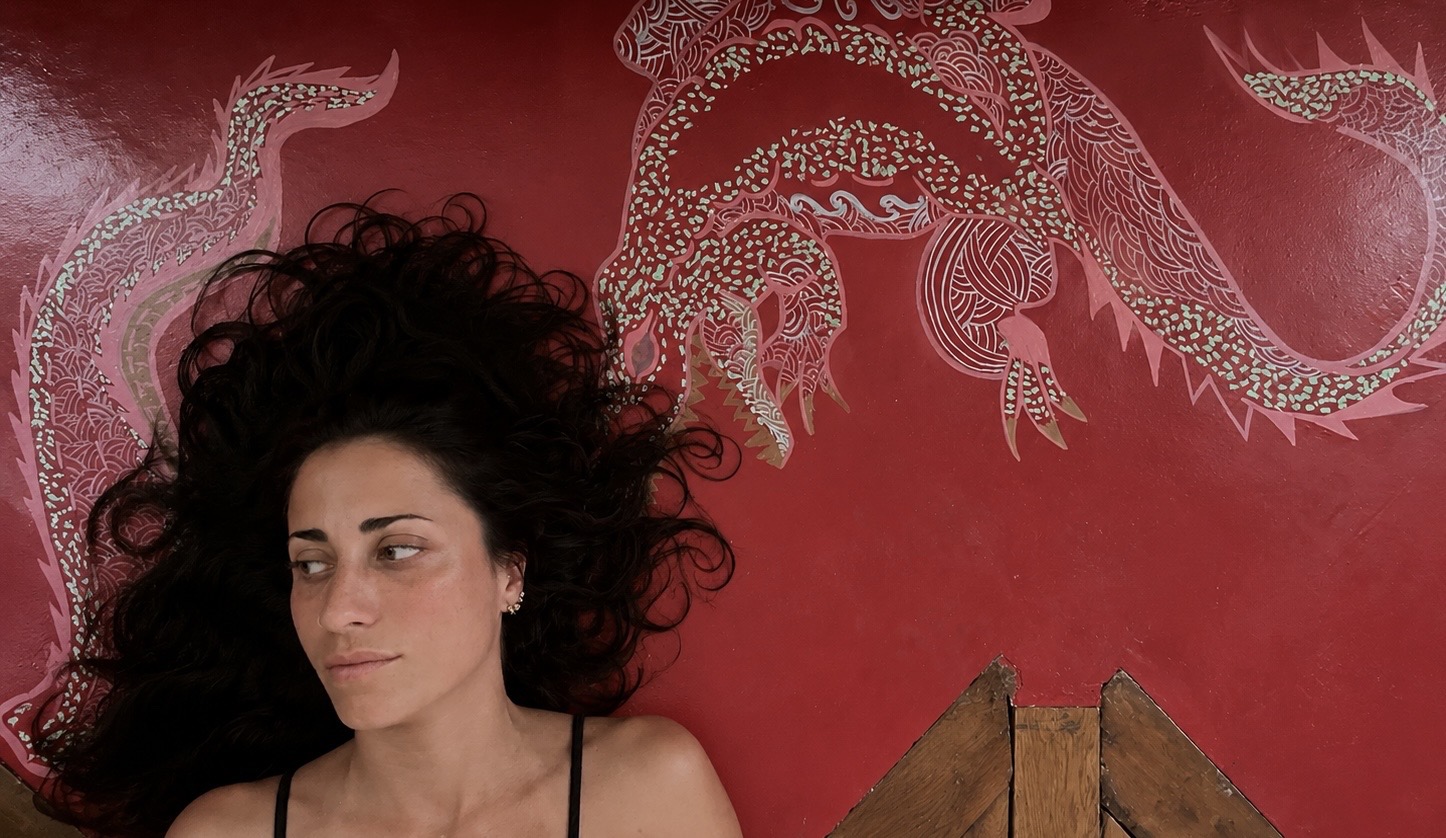 A woman lying below a red mural of a crocodile-like creature.