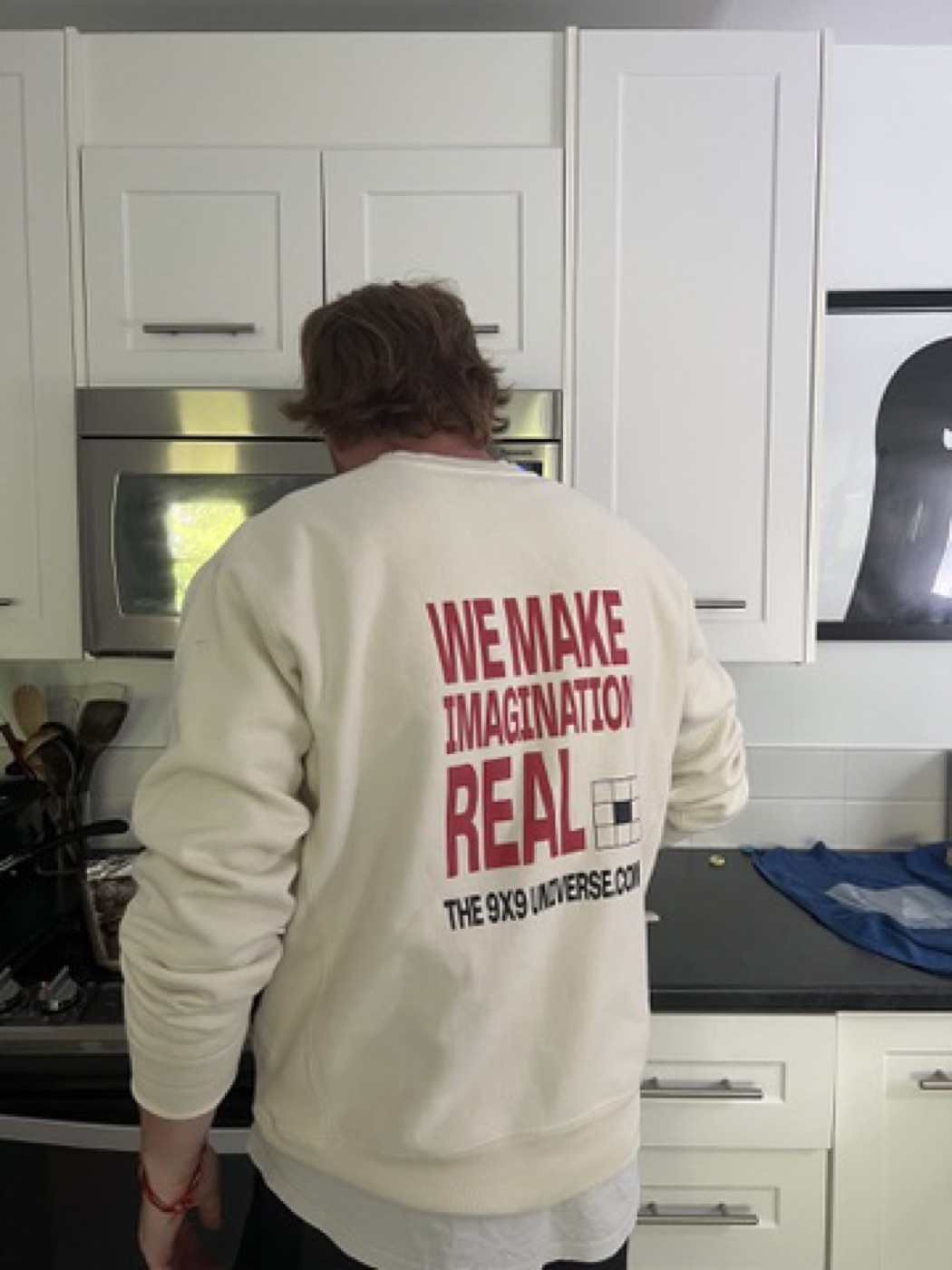 A cream 9x9 Universe crewneck worn in a kitchen.